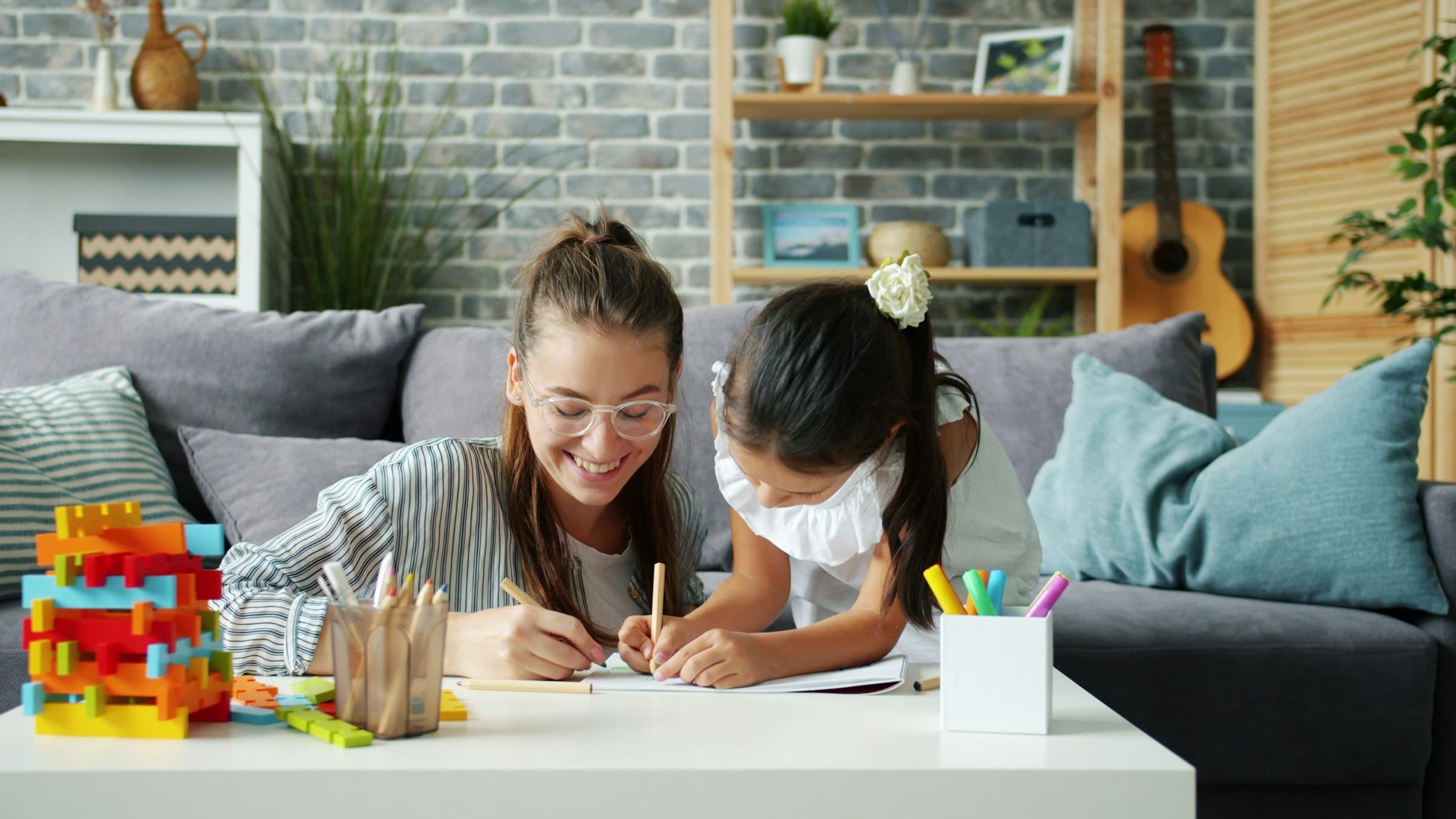 A woman and a young girl leaning over a notebook at a living-room table, drawing together with colored pencils